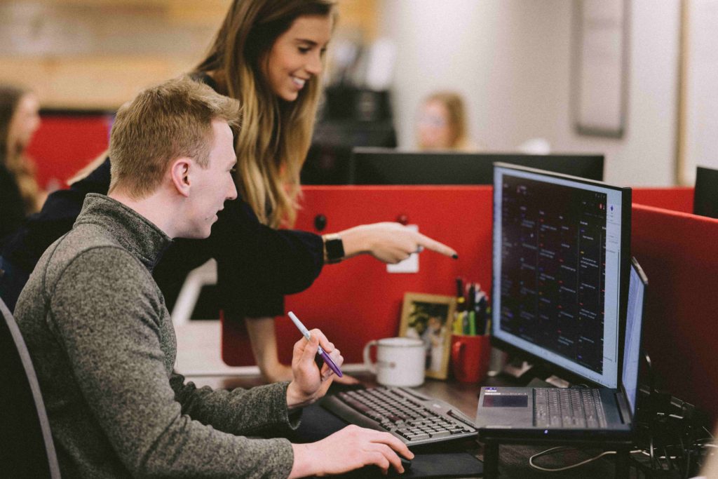 In the Magnetic North office, a coworker points to the computer screen while another sits and reviews it with them.
